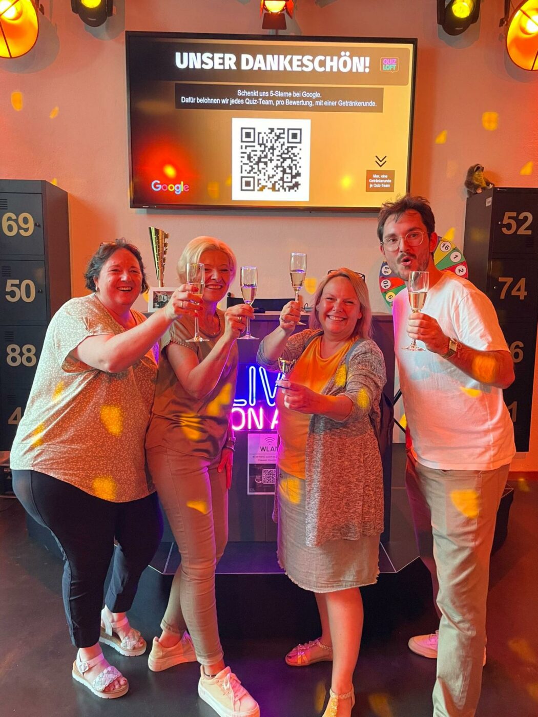 Drei Frauen und ein Mann stoßen mit Sekt auf ihren Sieg an